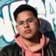 Portrait de Patrick Abrams, posé devant un mur tagué, portant un sweat rose et une veste noire